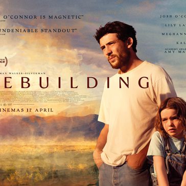 a man and a young girl standing together in a sunlit rural landscape with mountains in the background. The man, with short dark hair and light facial hair, looks off into the distance with a serious expression, while the girl stands close beside him, appearing thoughtful.