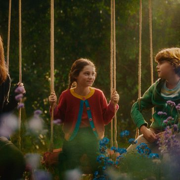 3 children all sat on swings in a forest.