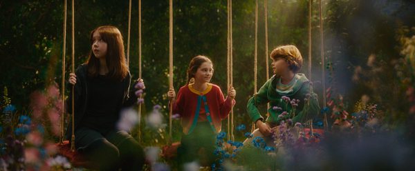 3 children all sat on swings in a forest.