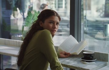 Zendaya reading a book looking towards camera.