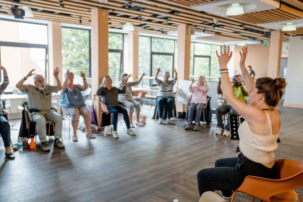 Lindsay with participants sat in chairs with their arms up.