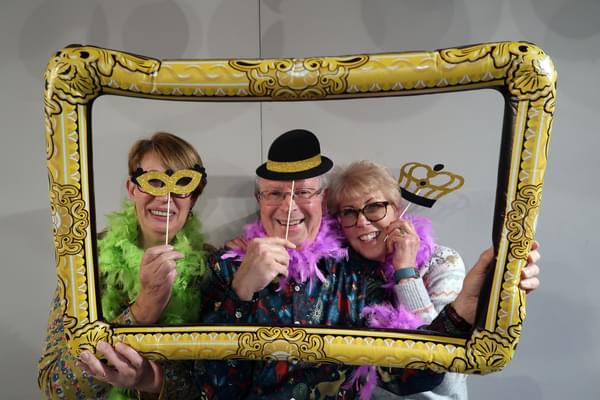 Three people stand within a novelty inflatable picture frame, smiling