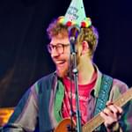 Sam holding a guitar with a happy birthday hat on.