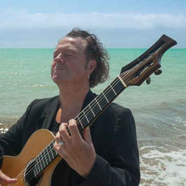 Richard holding a guitar by the sea.