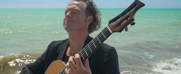 Richard holding a guitar by the sea.