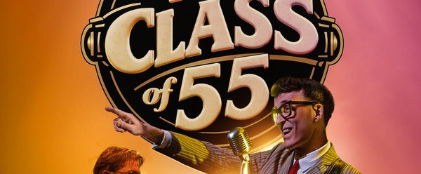 One man holding a guitar and singing with another man singing while playing the piano.