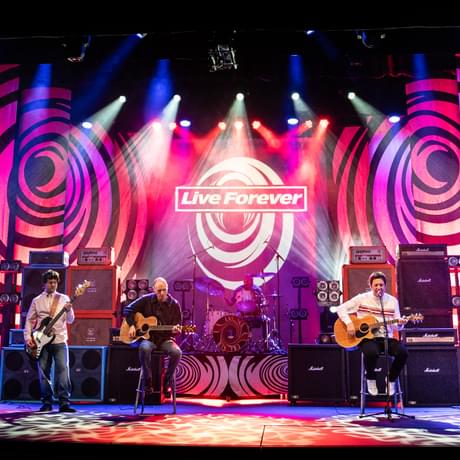 Live forever band on stage, brightly lit in hues of purples and pinks. There are swirl patterns on display