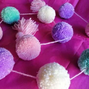 Multi-coloured pom poms attached together by string.