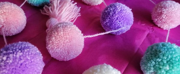 Multi-coloured pom poms attached together by string.