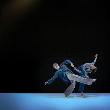 Two dancers dressed in casual blue clothes are centre stage under a cool light, they move with abandon, legs and heads throwing away from one another but their hands reach towards each other - desperate for connection.
