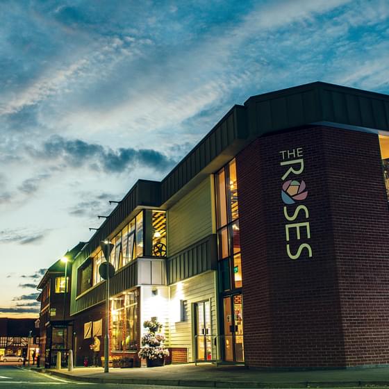 A view of The Roses' lit building against a striking dusky sky