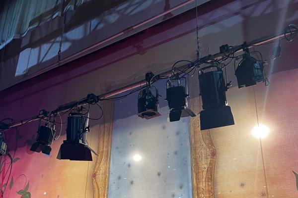 A theatre's lighting bars are lowered onto a stage, in front of a colourful pantomime backdrop